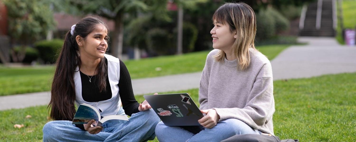 Two SPU students sit on the grass in the Tiffany Loop